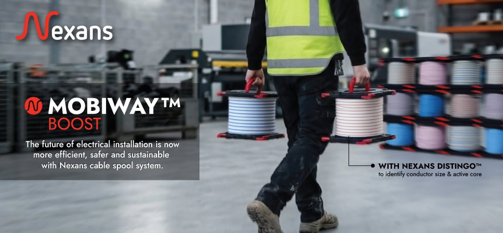 High-visibility worker carrying Nexans cable spools for electrical installation.