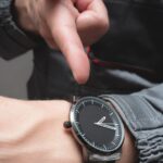 Wristwatch with black dial and silver case on person's wrist, close-up shot.