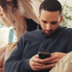 A man using a smartphone on a cozy sofa in a modern living room.