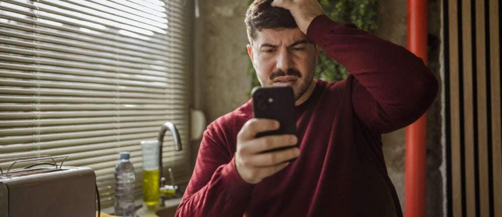 Anxious man looking at smartphone in a modern office setting.