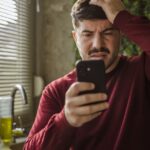 Anxious man looking at smartphone in a modern office setting.