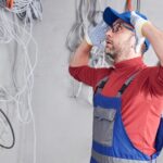 Electrical technician inspecting wiring on a wall with tangled cables in the background.